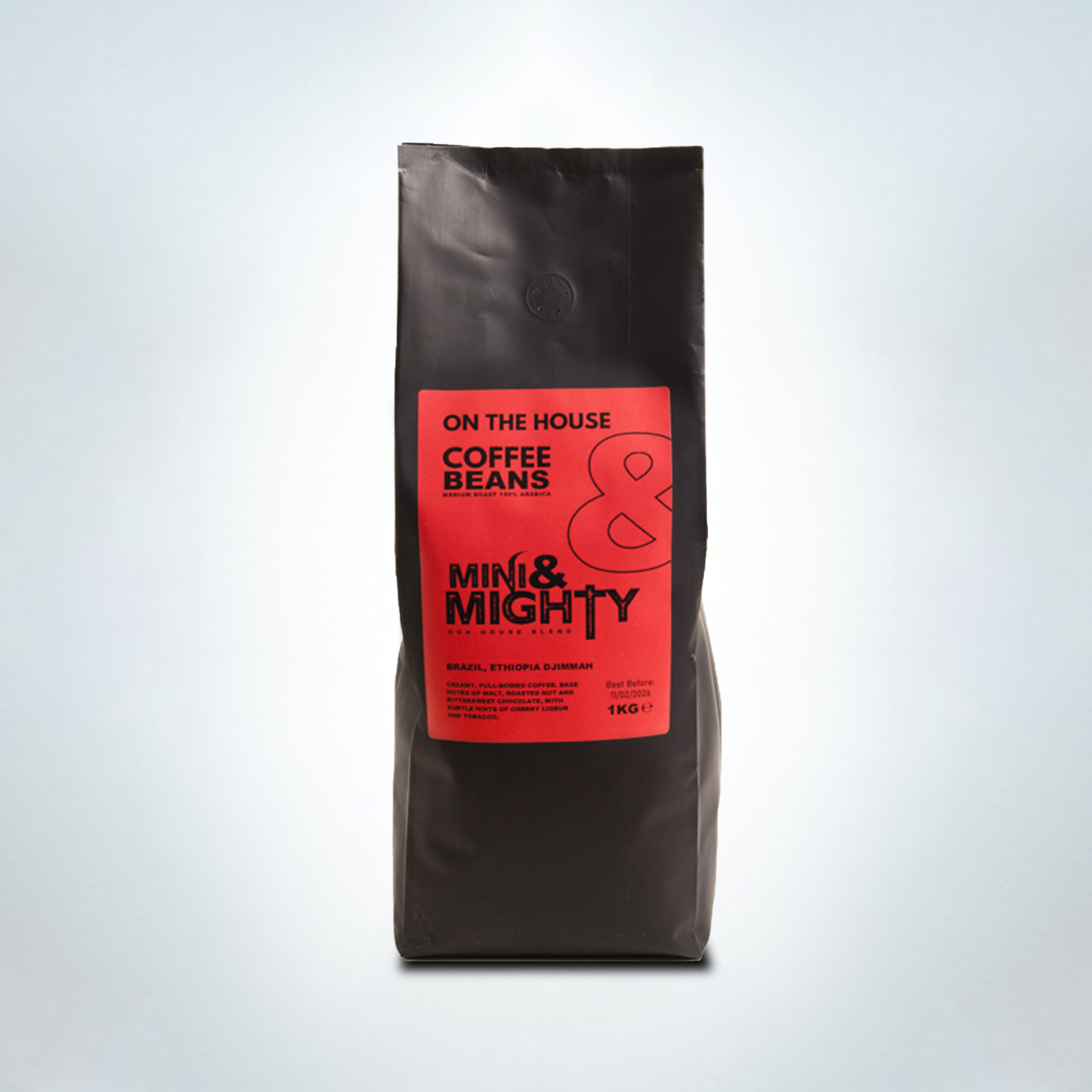 1kg bag of Mini & Mighty “On The House” coffee beans with a bold red label. A medium roast 100% Arabica blend from Brazil and Ethiopia Djimmah, featuring creamy, full-bodied notes of malt, roasted nut, bittersweet chocolate, cherry liqueur, and tobacco.