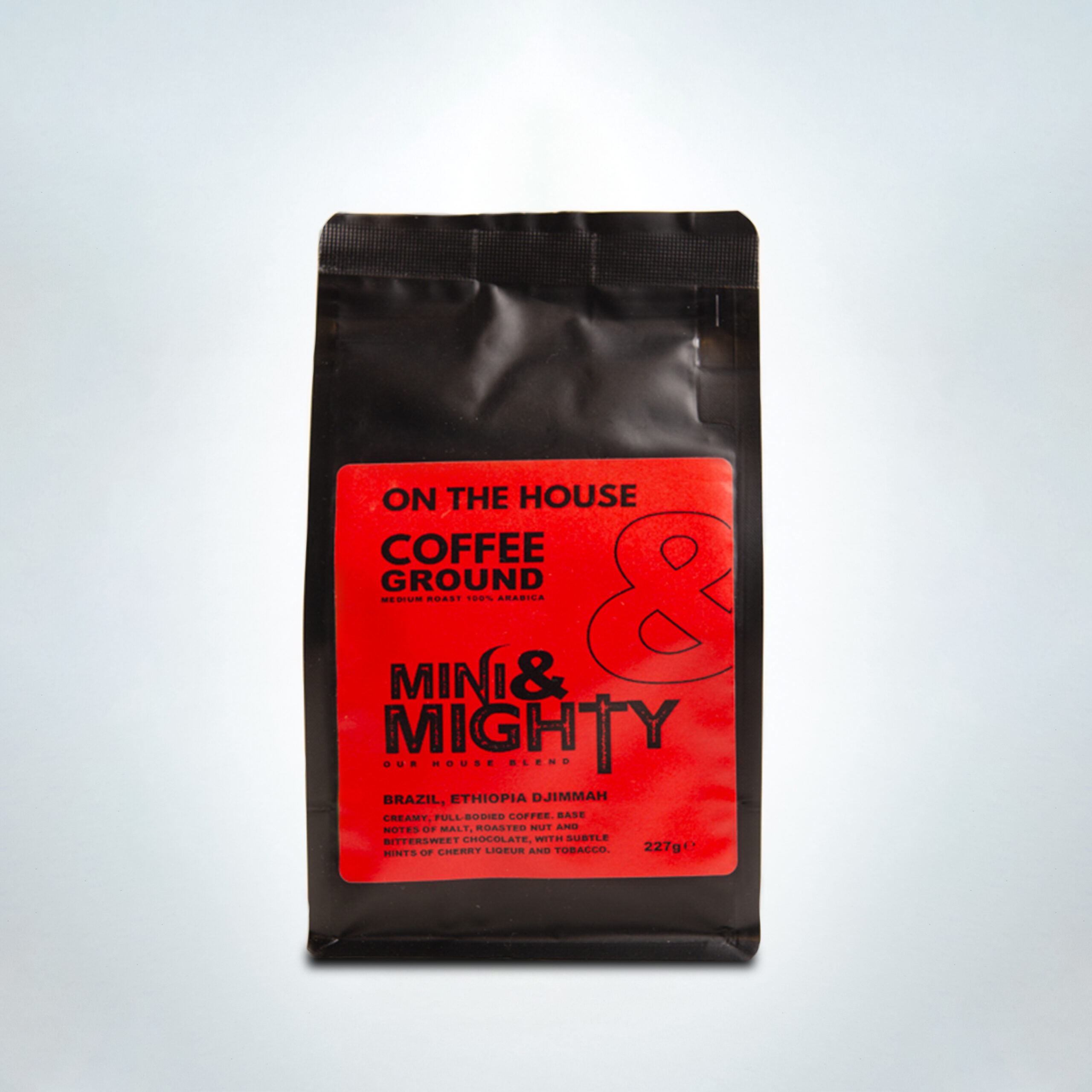 227g bag of Mini & Mighty “On The House” ground coffee in red packaging. A medium roast 100% Arabica blend from Brazil and Ethiopia Djimmah, offering creamy, full-bodied flavour with notes of malt, roasted nut, bittersweet chocolate, cherry liqueur, and tobacco.
