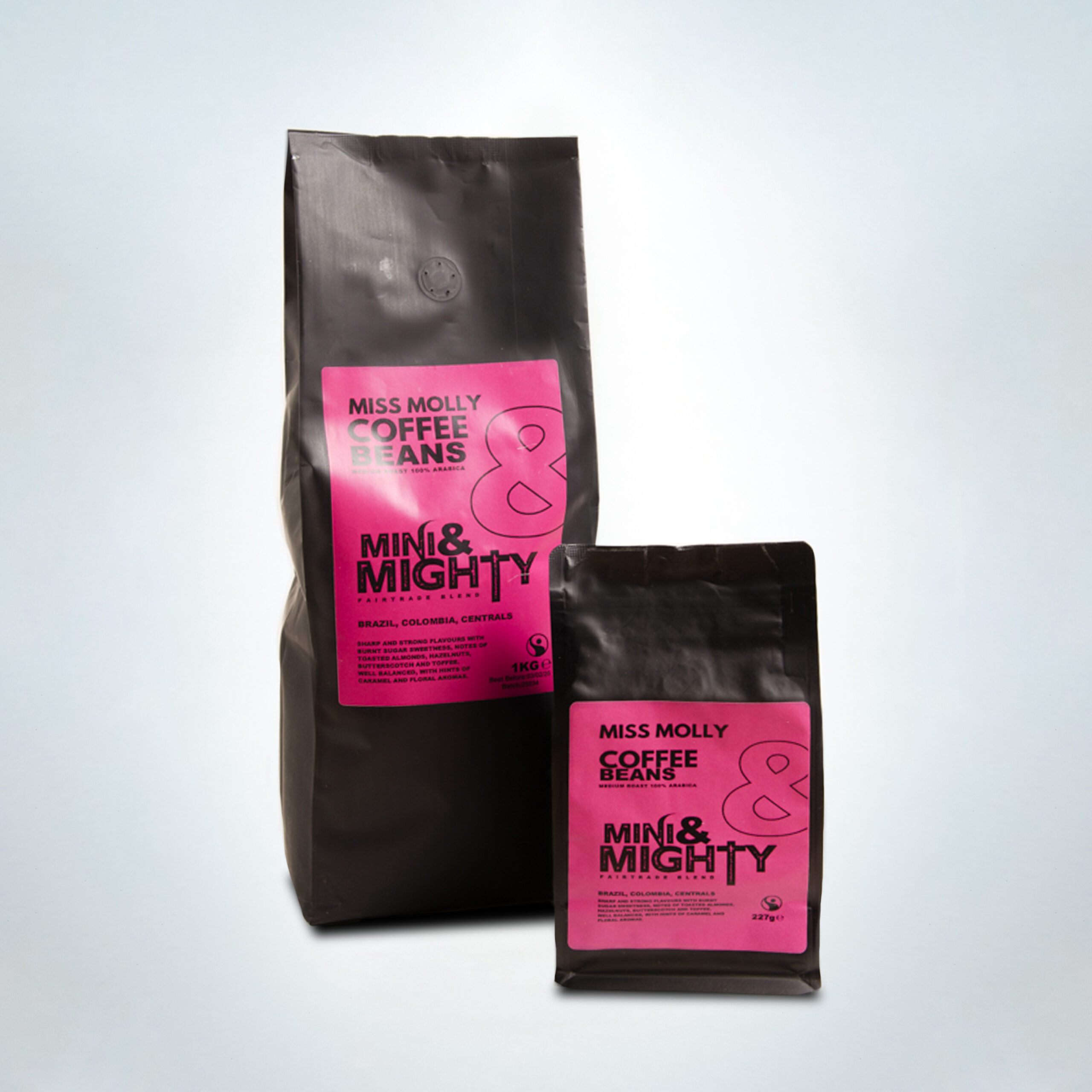 Two Mini & Mighty “Miss Molly” Fairtrade coffee bags — a 1kg and a 227g pack — with vibrant pink labels. Medium roast 100% Arabica blend from Brazil, Colombia, and Central America featuring bold flavours of burnt sugar, almonds, hazelnuts, butterscotch, and floral caramel notes.