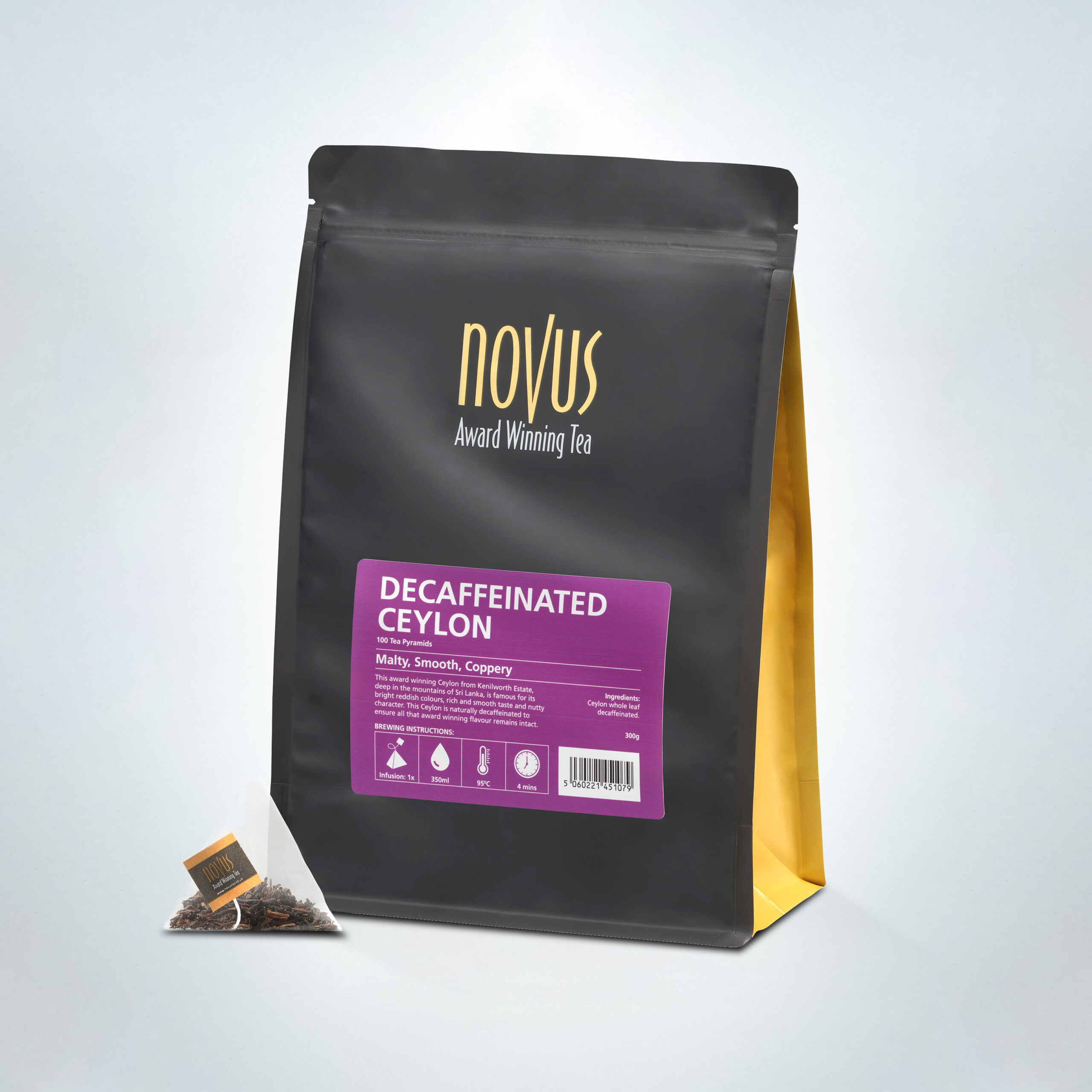 Novus Award Winning Decaffeinated Ceylon Tea in a 100-pyramid bag pack, featuring malty, smooth, and coppery flavor notes, shown with a single pyramid tea bag and sleek black and gold packaging