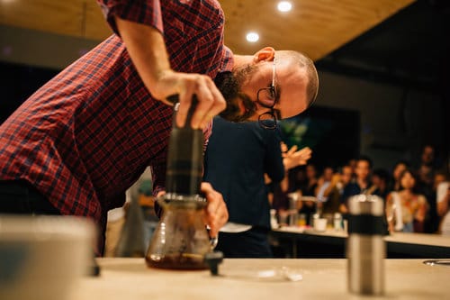 Barista proudly holding an Aeropress coffee maker, showcasing its sleek design and versatility for brewing rich coffee with precision