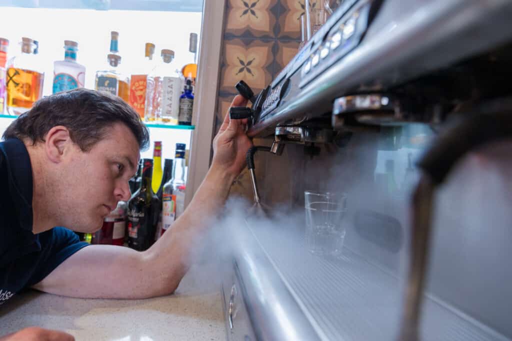 Barista serving a freshly made espresso drink with professional coffee equipment, showcasing high-quality beverage preparation in a café setting