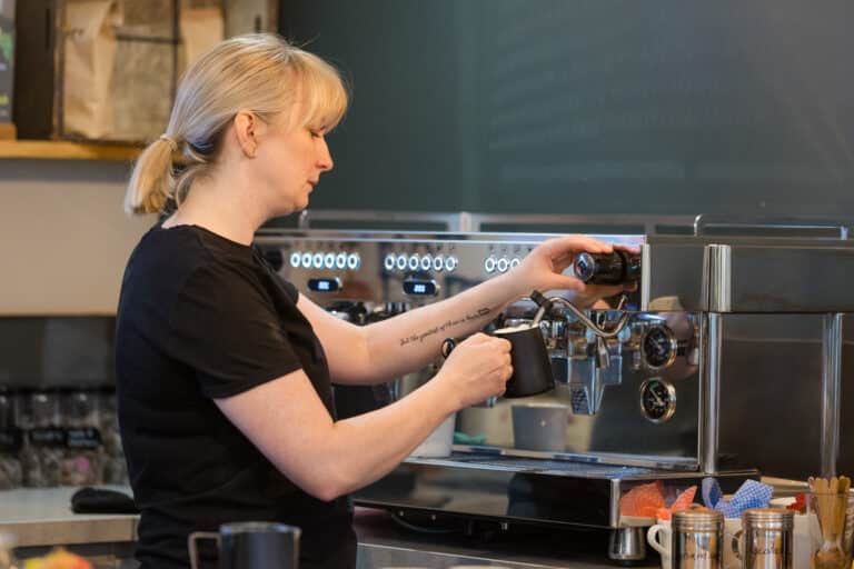 Barista at Bridge Coffee, Bolton, preparing Mini & Mighty coffee using a professional espresso machine, demonstrating precision and technique in a café environment